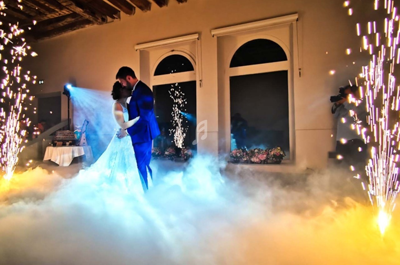 Un couple danse au milieu d'une scène éclairée par des étincelles et entourée de fumée dans une salle élégante.