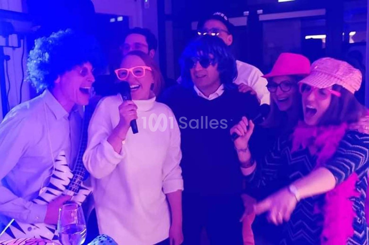 Des personnes déguisées chantent et s'amusent dans une ambiance festive avec éclairage coloré.