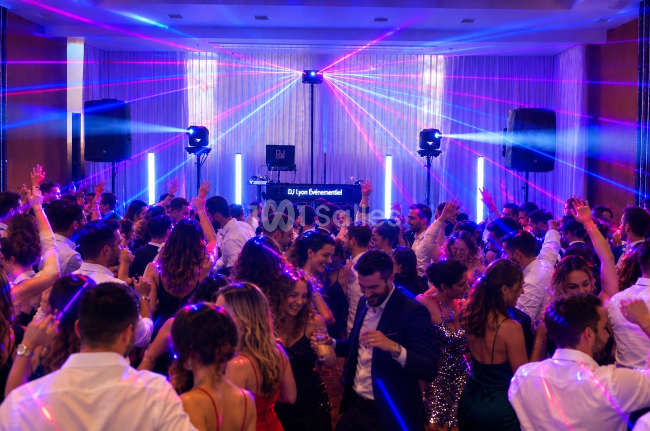 Salle animée par un DJ avec éclairage laser rose et bleu, piste de danse remplie de convives.