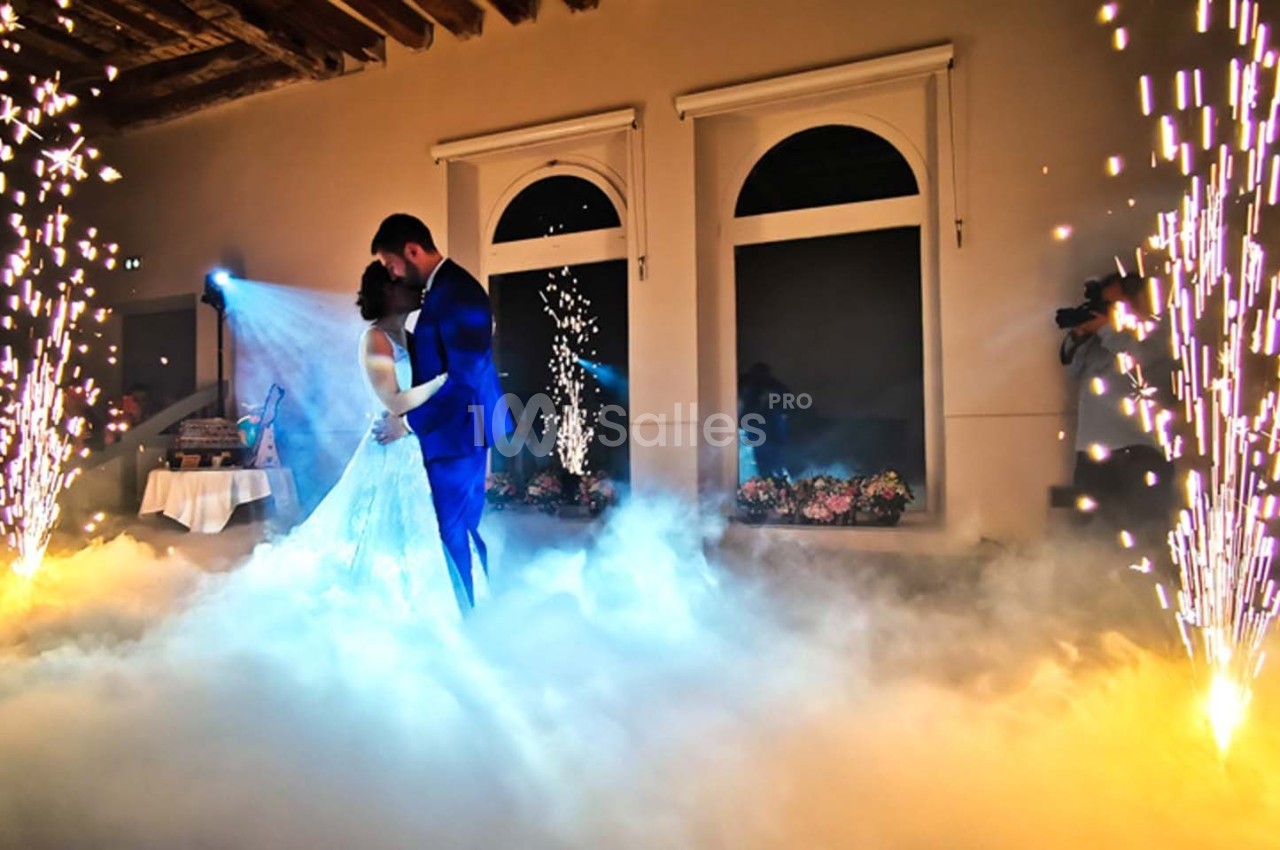 Un couple danse au milieu d'une scène éclairée par des étincelles et entourée de fumée dans une salle élégante.