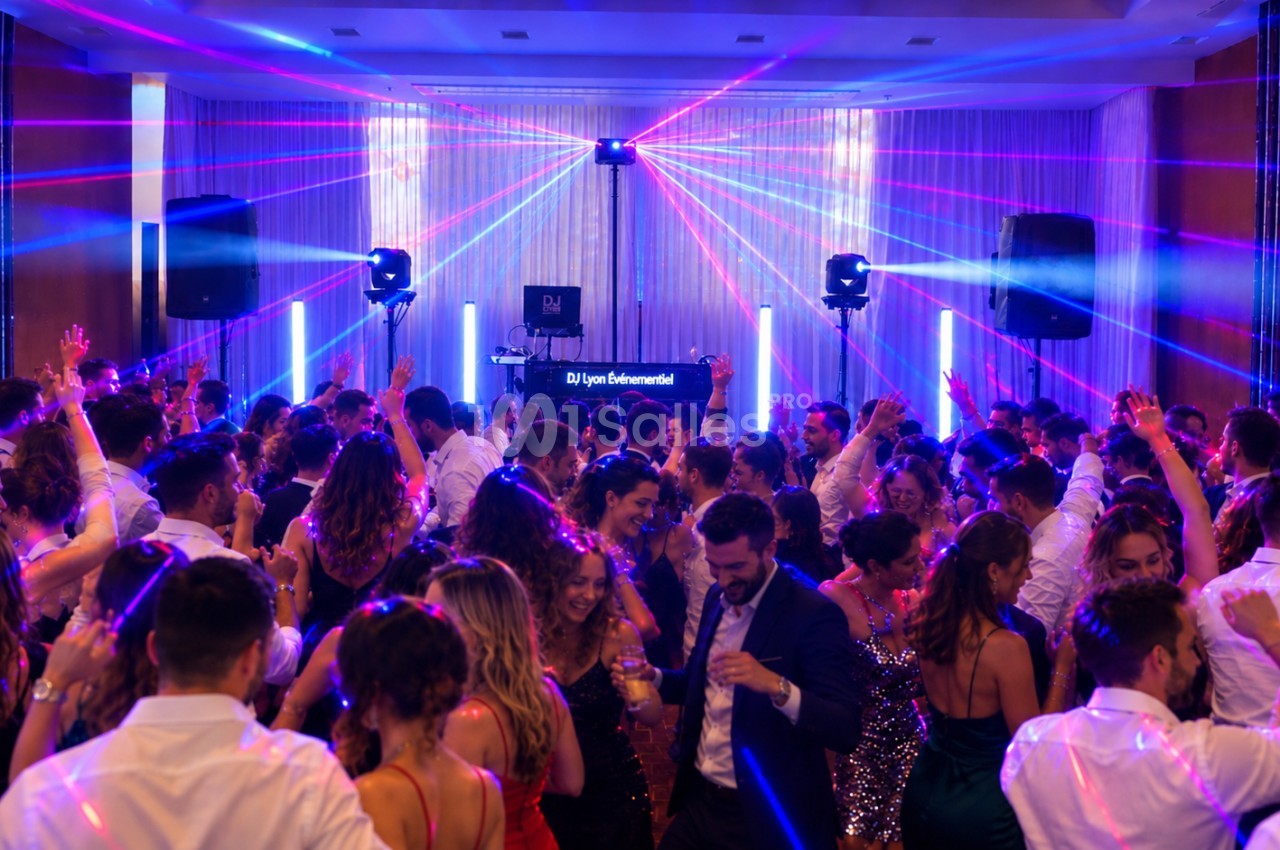 Salle animée par un DJ avec éclairage laser rose et bleu, piste de danse remplie de convives.