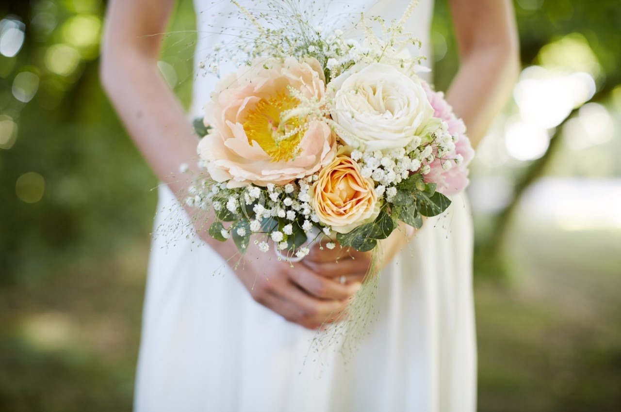 Une mariée en robe blanche tenant un bouquet de fleurs pastel avec des touches de gypsophile.