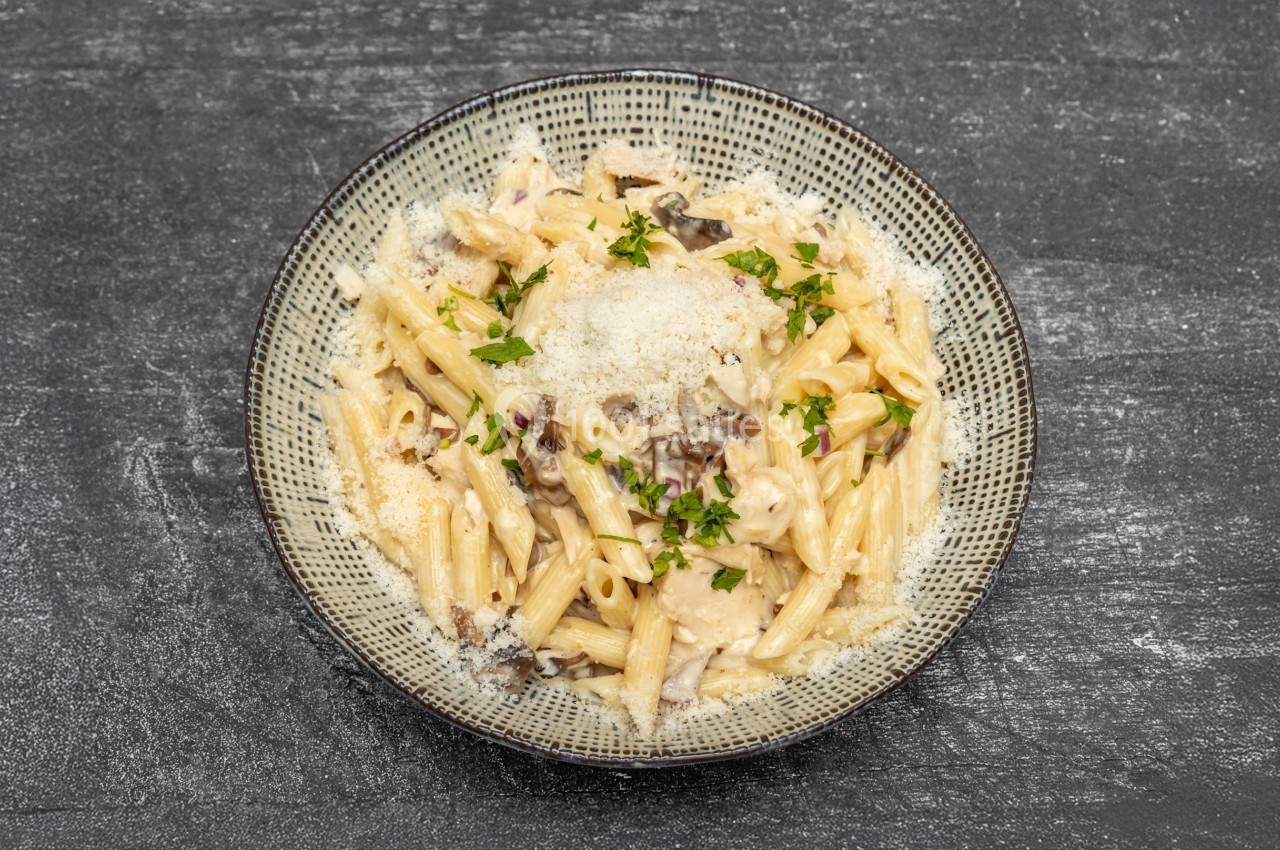 Assiette de pâtes crémeuses garnies de champignons, persil frais et fromage râpé, sur une table sombre.