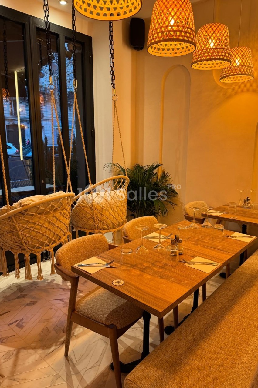 Salle de restaurant chaleureuse avec table en bois, chaises, banquette, balançoires suspendues et éclairage tamisé.