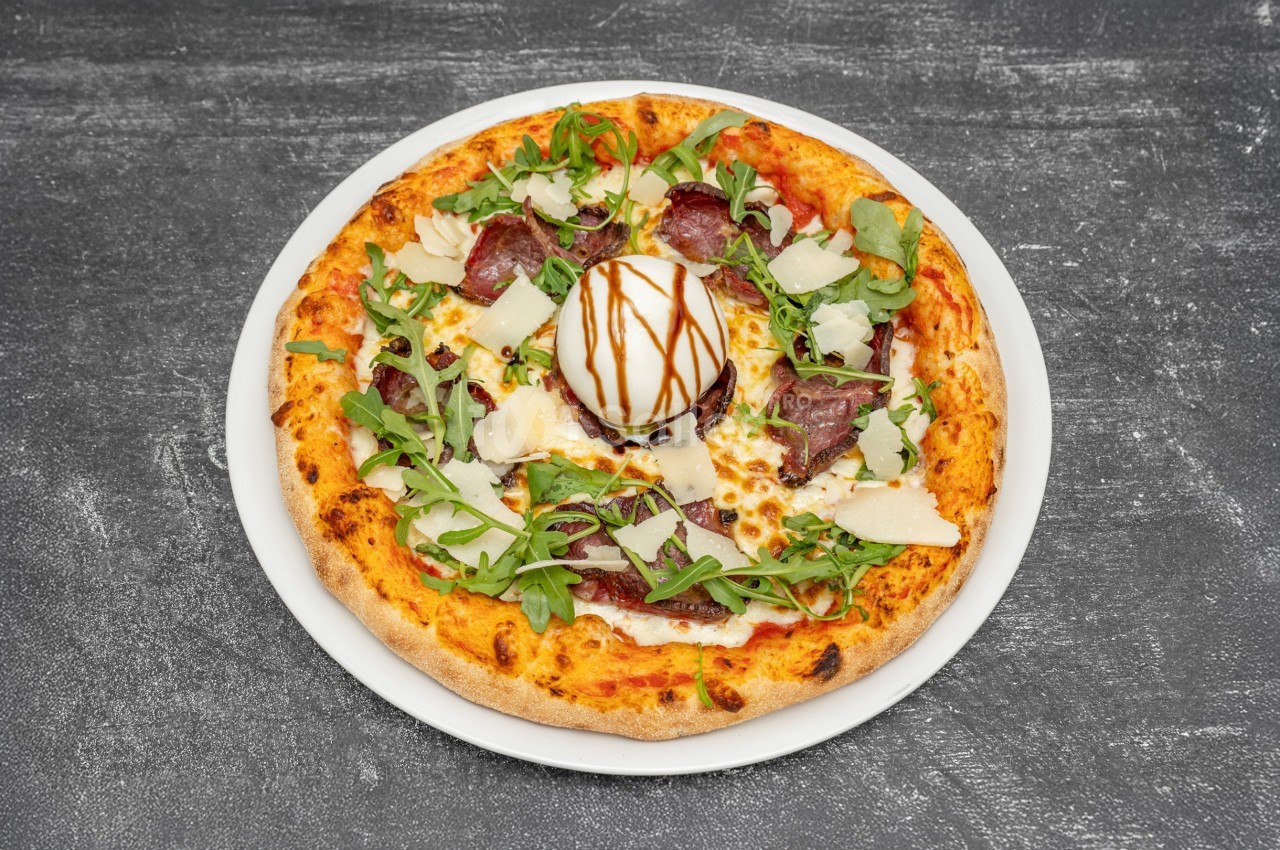 Pizza garnie de roquette, bresaola, copeaux de parmesan, burrata au centre et filet de vinaigre balsamique.