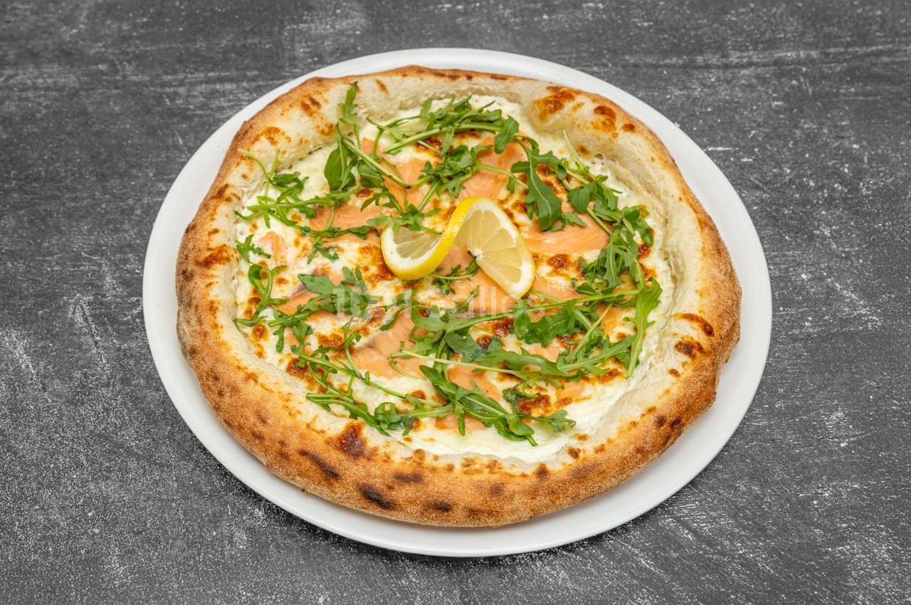 Pizza garnie de saumon fumé, roquette, citron et fromage, servie sur une assiette blanche sur fond gris.