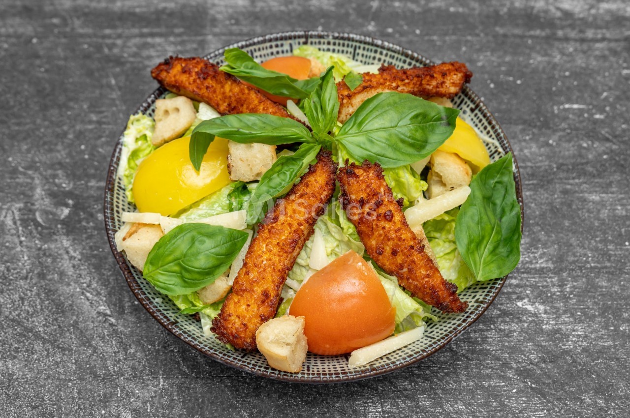 Assiette de salade composée avec tomates, poivrons jaunes, croûtons, filets de poulet panés et feuilles de basilic.