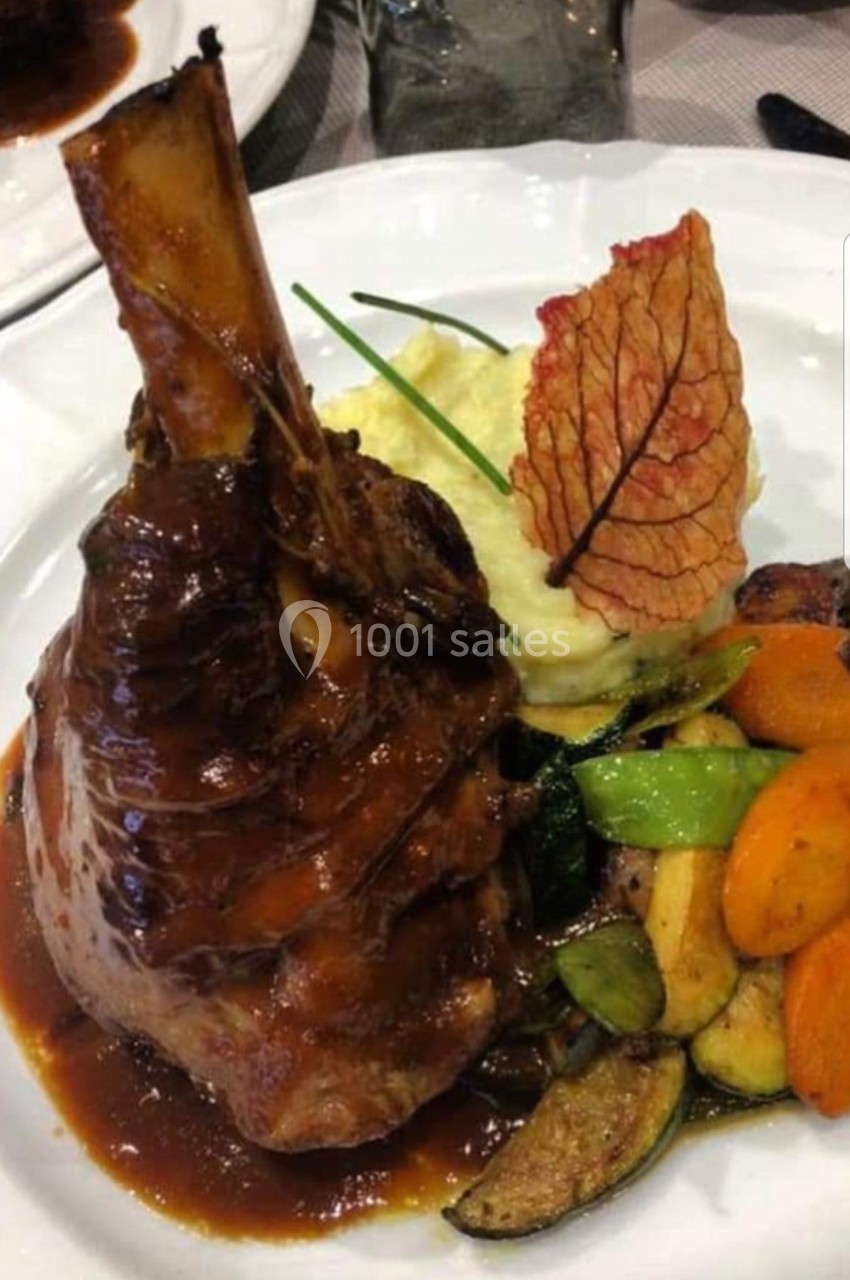 Jarret d'agneau braisé avec sauce, purée de pommes de terre, légumes sautés et décoration de feuille croustillante.