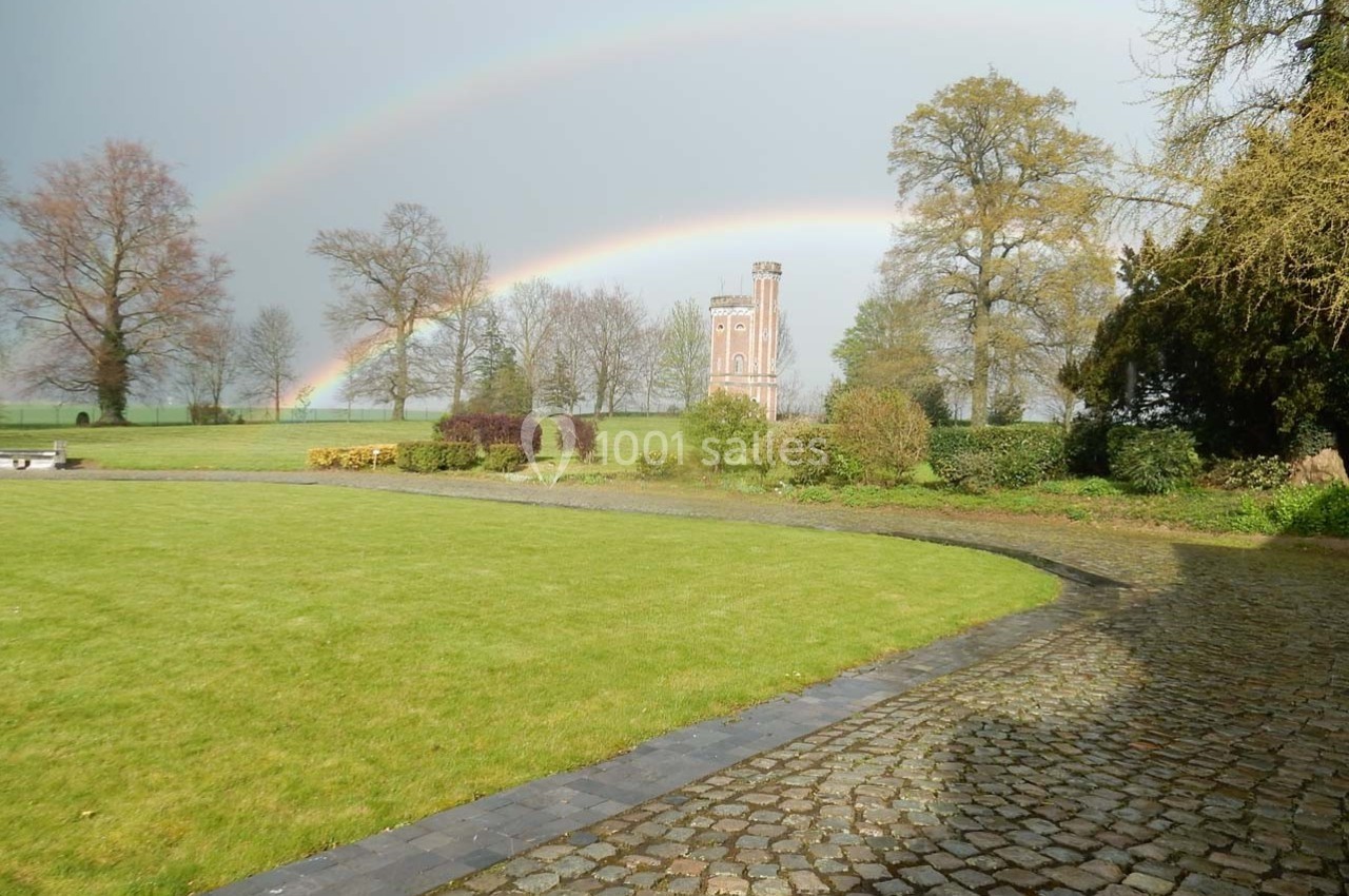 Deux arcs-en-ciel au-dessus d'un parc verdoyant avec une tour en briques entourée d'arbres.