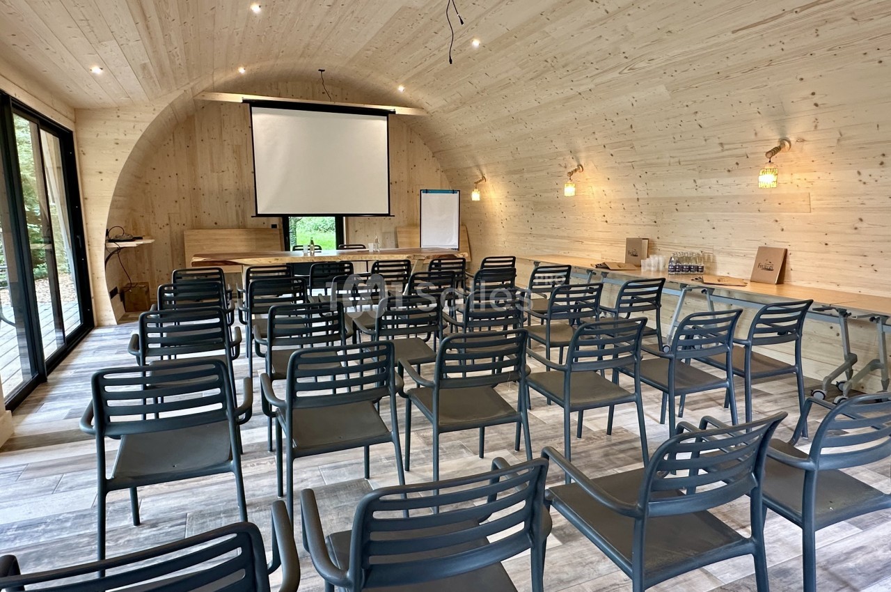 Salle de réunion en bois avec des rangées de chaises, un écran de projection, un paperboard et des fenêtres donnant sur l…