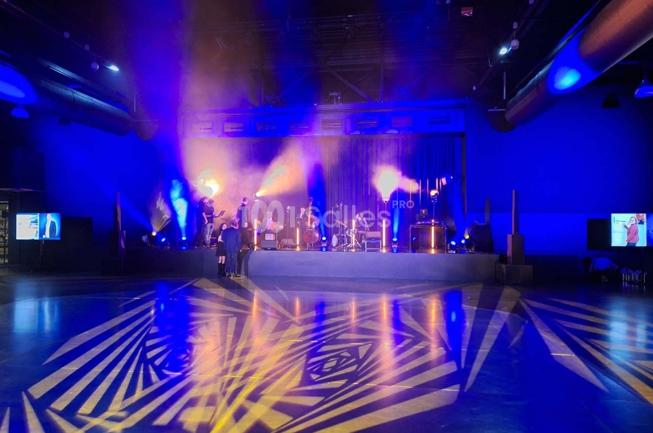 Scène illuminée avec des projecteurs colorés dans une salle sombre, décor géométrique au sol.