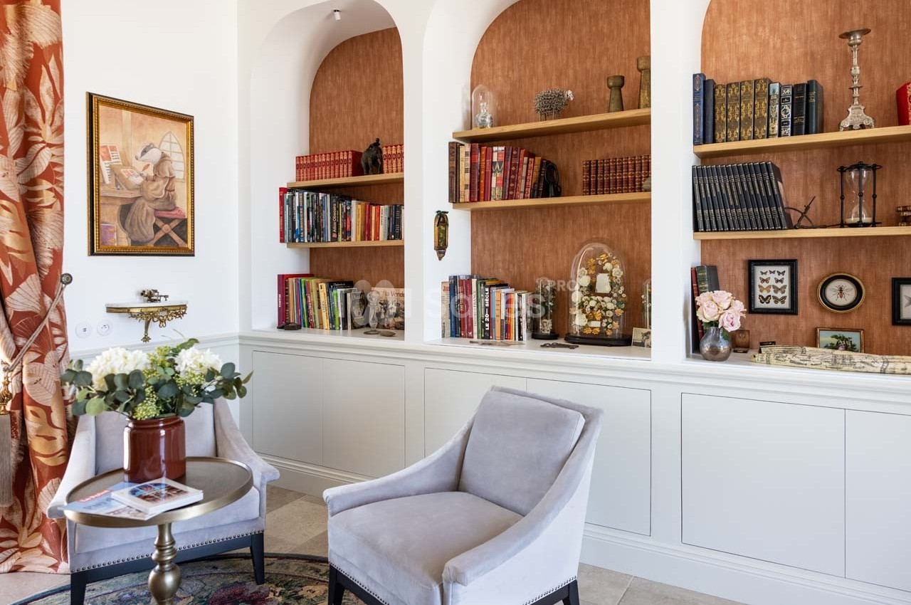 Bibliothèque intégrée avec étagères en bois, livres, objets décoratifs et deux fauteuils dans un salon lumineux.