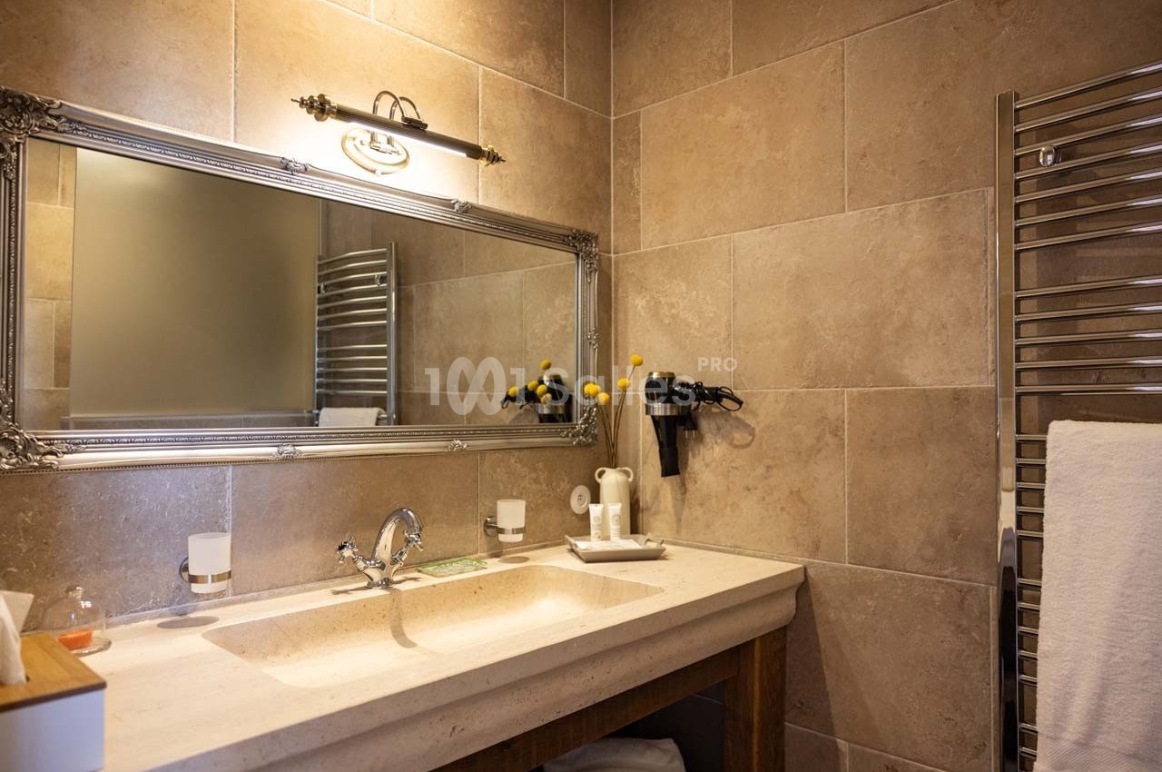 Salle de bain avec lavabo, grand miroir, porte-serviettes chauffant et mur en carrelage beige.