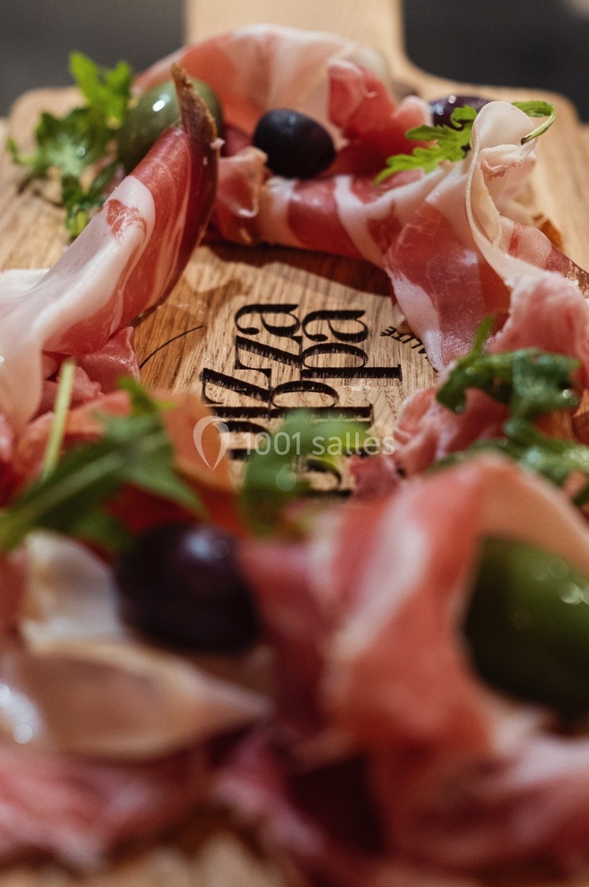 Plateau en bois garni de tranches de jambon cru, olives vertes et noires, et feuilles de roquette.