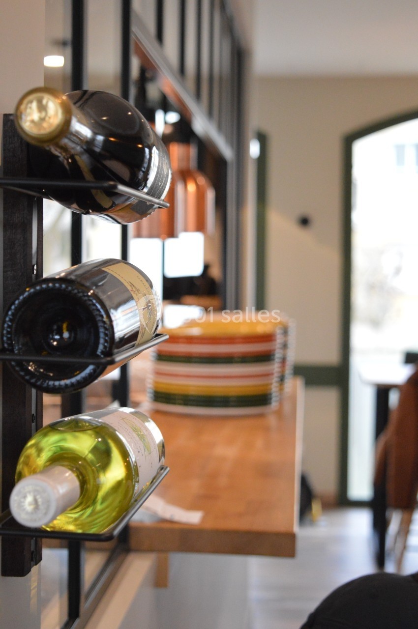 Bouteilles de vin rangées horizontalement sur un support mural dans un intérieur lumineux avec une table en bois.