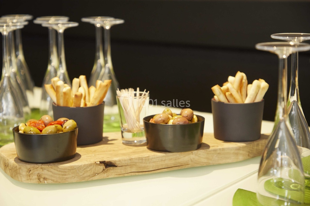 Assortiment d'olives, gressins et piques en bois disposés sur une planche en bois, entourés de verres à pied.