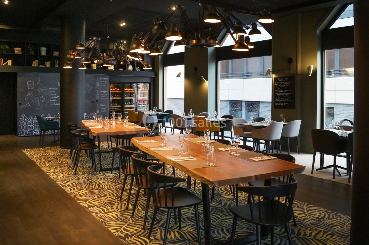 Salle de restaurant moderne avec tables en bois, chaises noires et éclairage suspendu, donnant sur des baies vitrées.