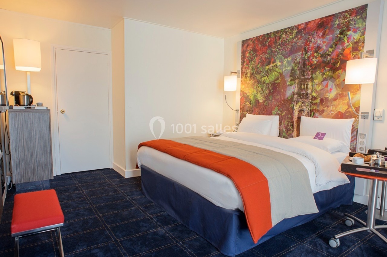 Chambre d'hôtel avec lit double, décoration colorée au mur, éclairage doux et mobilier moderne.
