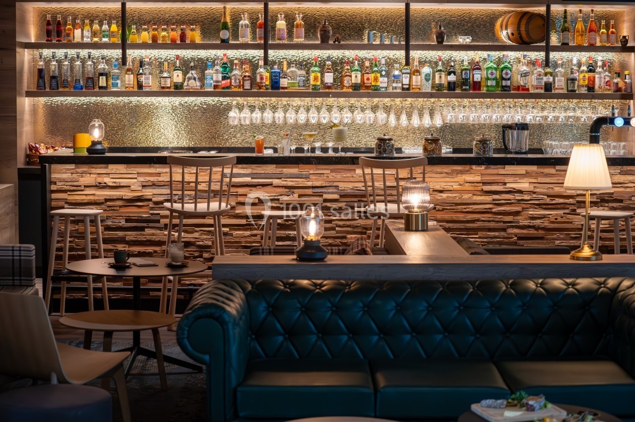 Bar élégant avec comptoir en pierre, étagères remplies de bouteilles, tabourets et ambiance lumineuse chaleureuse.