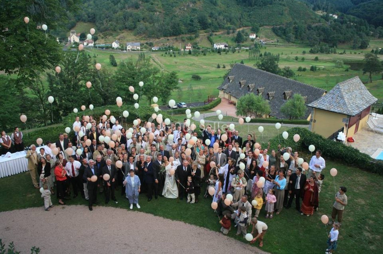 Groupe de personnes rassemblées en extérieur, tenant des ballons prêts à être lâchés, avec un paysage verdoyant en arrière…