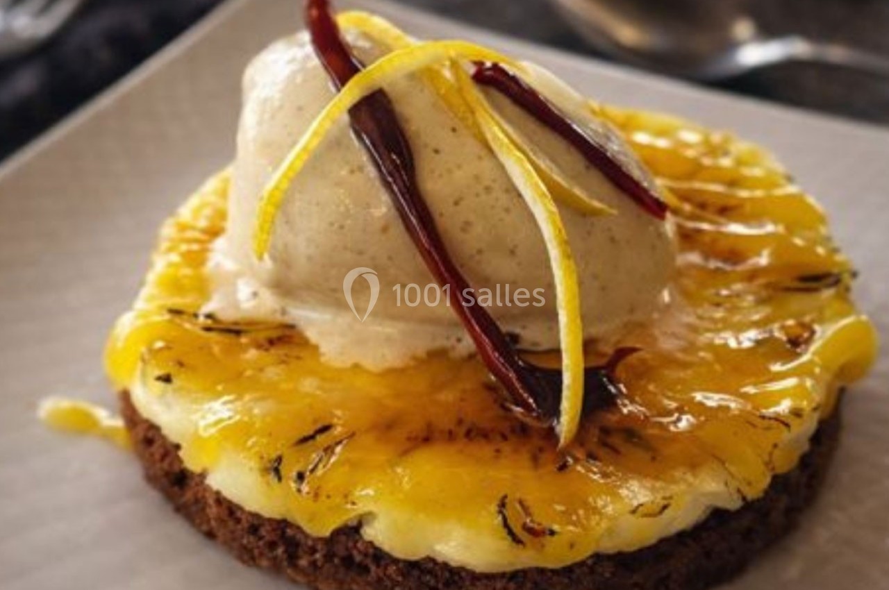 Tranche d'ananas grillée sur un biscuit, garnie de glace vanille, zestes de citron et piments rouges décoratifs.