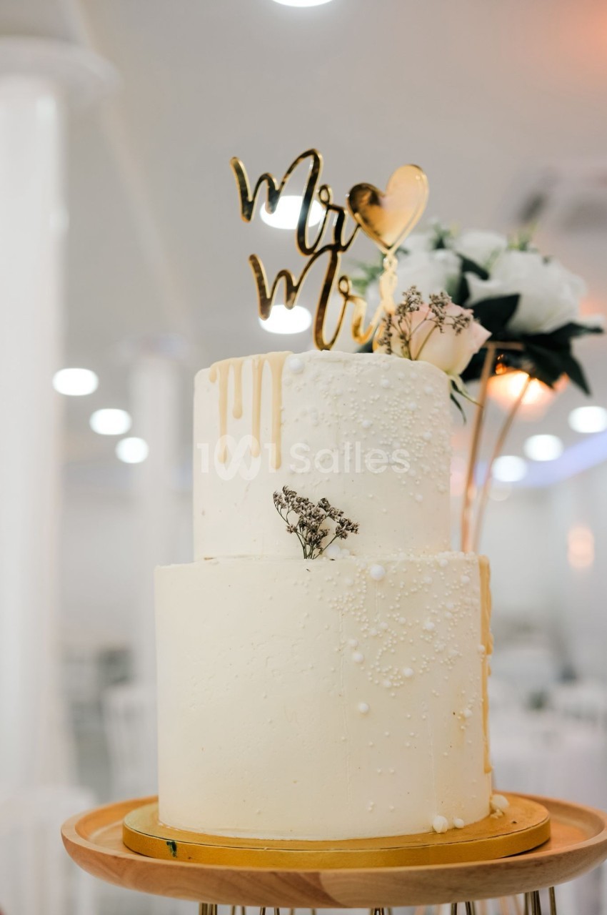 Gâteau de mariage à deux étages décoré de perles comestibles, fleurs et un topper ’Mr & Mrs’.