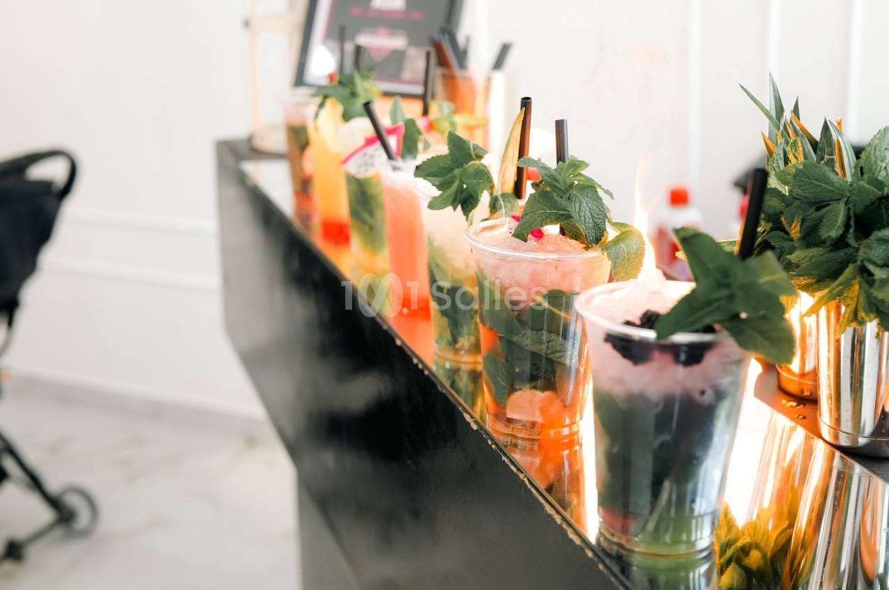 Verres de cocktails colorés garnis de feuilles de menthe, alignés sur un comptoir noir brillant.