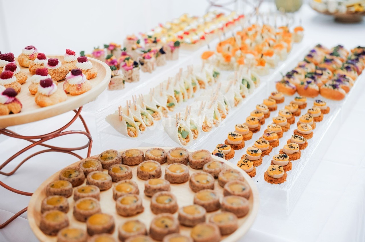 Plateaux de bouchées apéritives variées disposées sur une table blanche, comprenant canapés, mini-sandwichs et amuse-bouches.