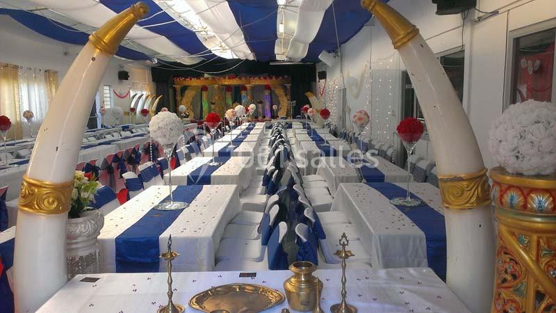 Salle décorée pour un événement avec longues tables dressées, nappes blanches et bleues, et ornements floraux.