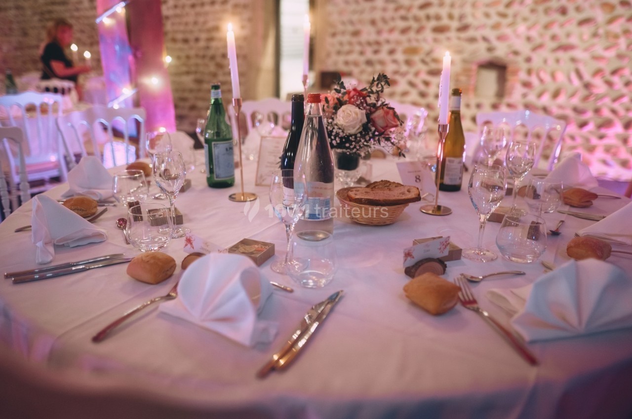 Table de réception dressée avec nappes blanches, verres, couverts, bougies, paniers de pain et décorations florales.