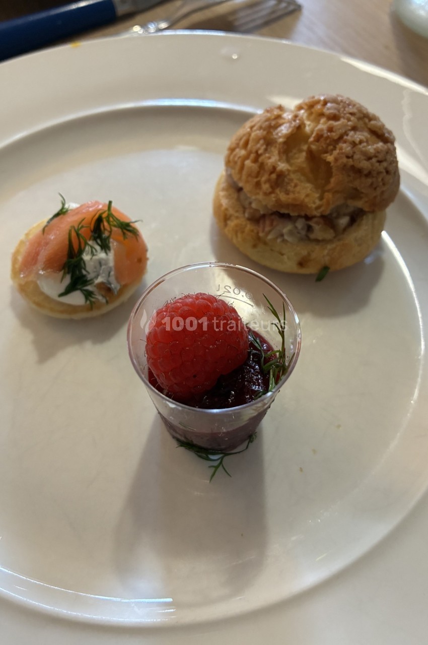 Assortiment de trois amuse-bouches : verrine aux fruits rouges, tartelette au saumon et choux garni sur une assiette blanche.