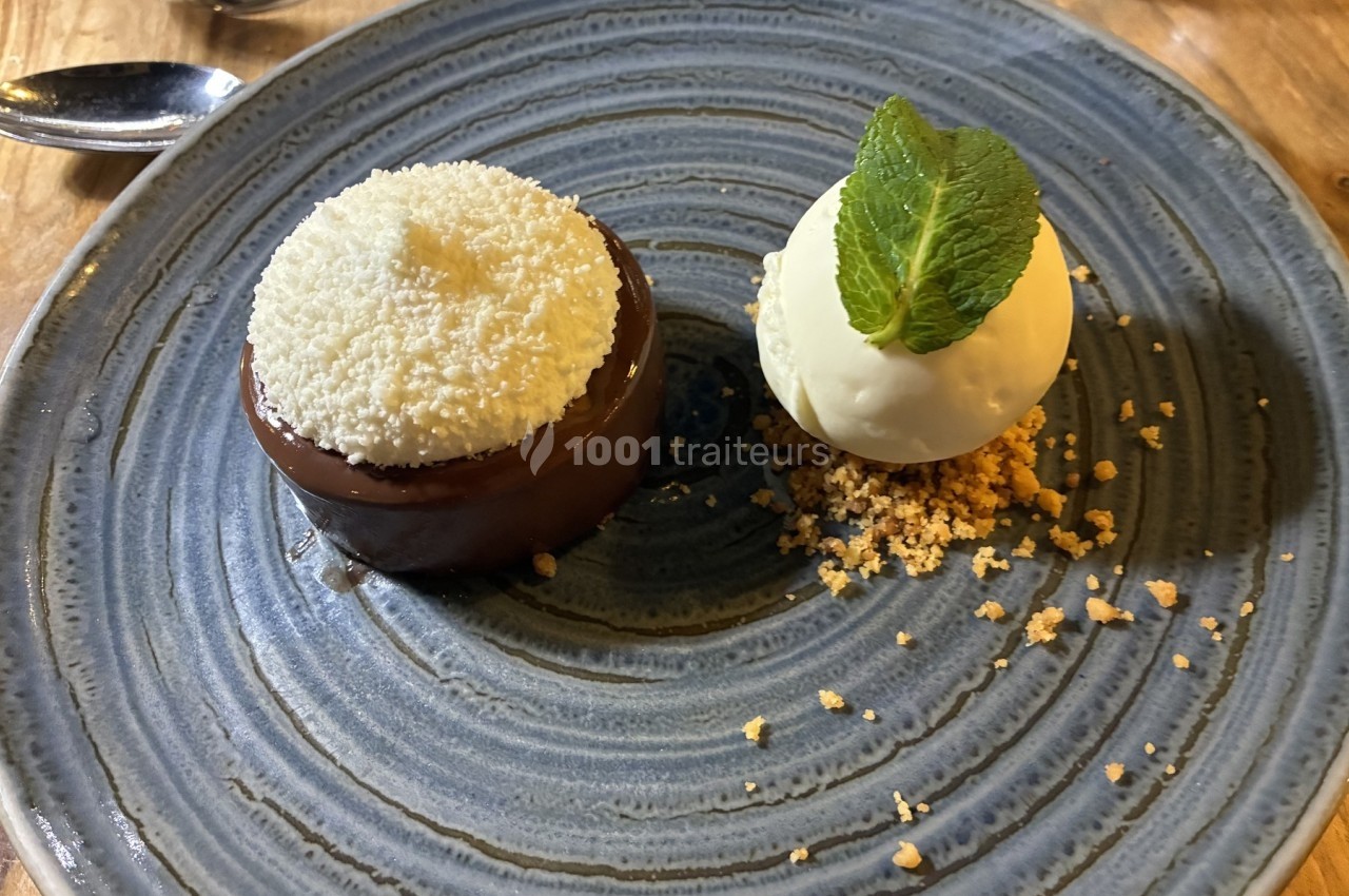 Dessert composé d'un gâteau au chocolat avec une garniture blanche et d'une boule de glace sur un lit de crumble.