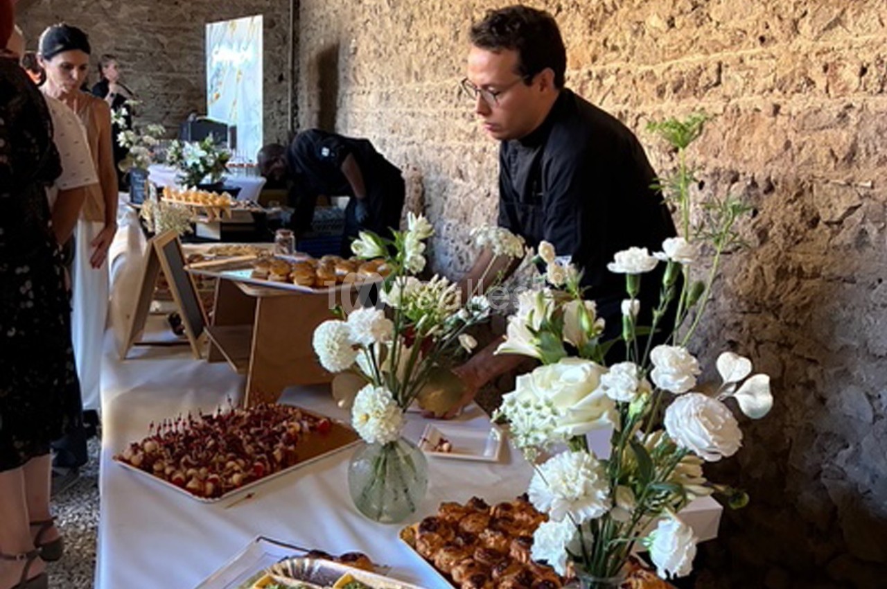 Un traiteur prépare un buffet avec des fleurs blanches en décoration dans une salle en pierre.