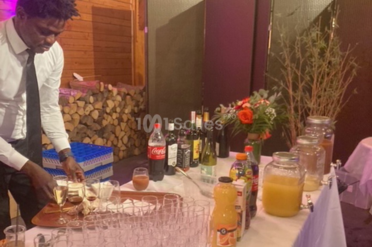 Un serveur prépare des verres de champagne sur un plateau, devant une table garnie de boissons et de décorations.