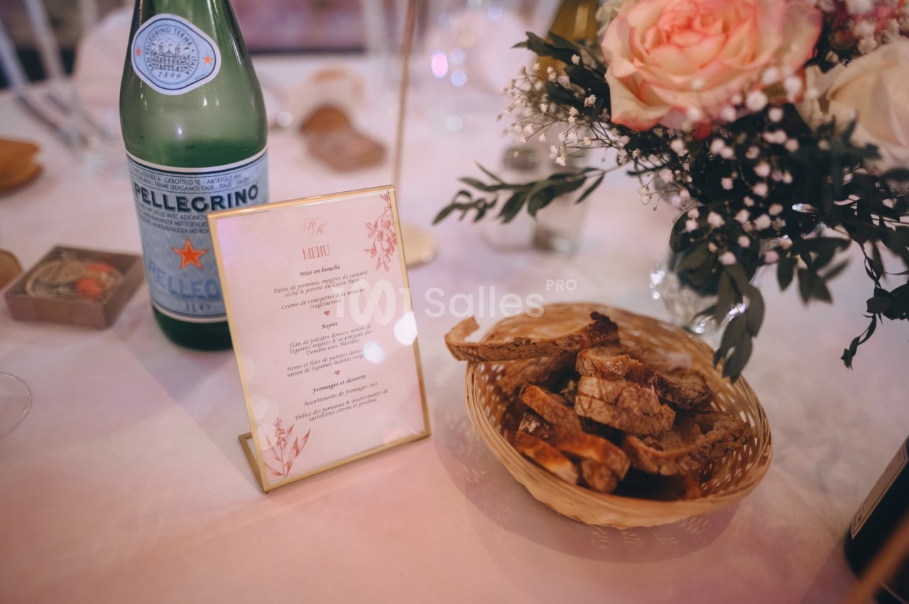 Bouteille d'eau, menu, panier de pain et bouquet de fleurs disposés sur une table dressée.