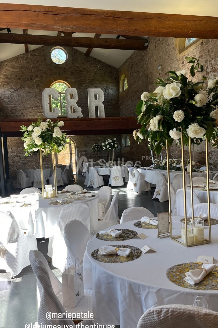 Salle de réception décorée avec des tables rondes, nappes blanches, compositions florales et initiales géantes en fond.