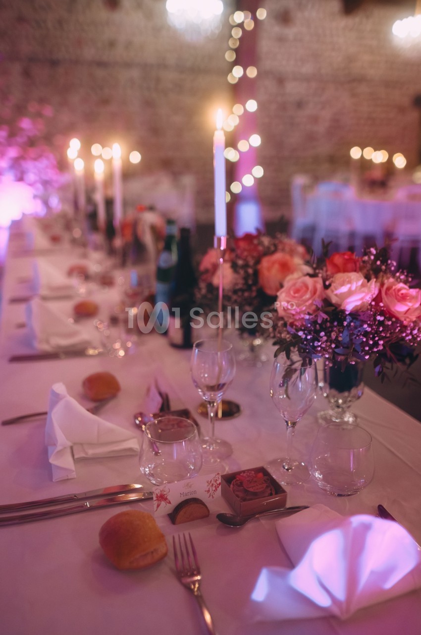 Table de réception élégamment dressée avec bougies, fleurs roses, verres et couverts dans une ambiance tamisée.