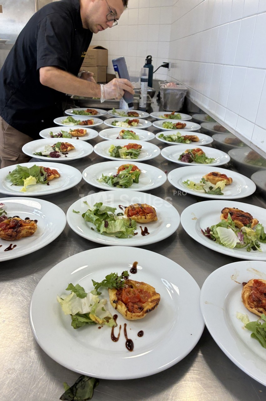 Un chef prépare des assiettes contenant des tartelettes aux légumes et de la salade verte dans une cuisine professionnelle.