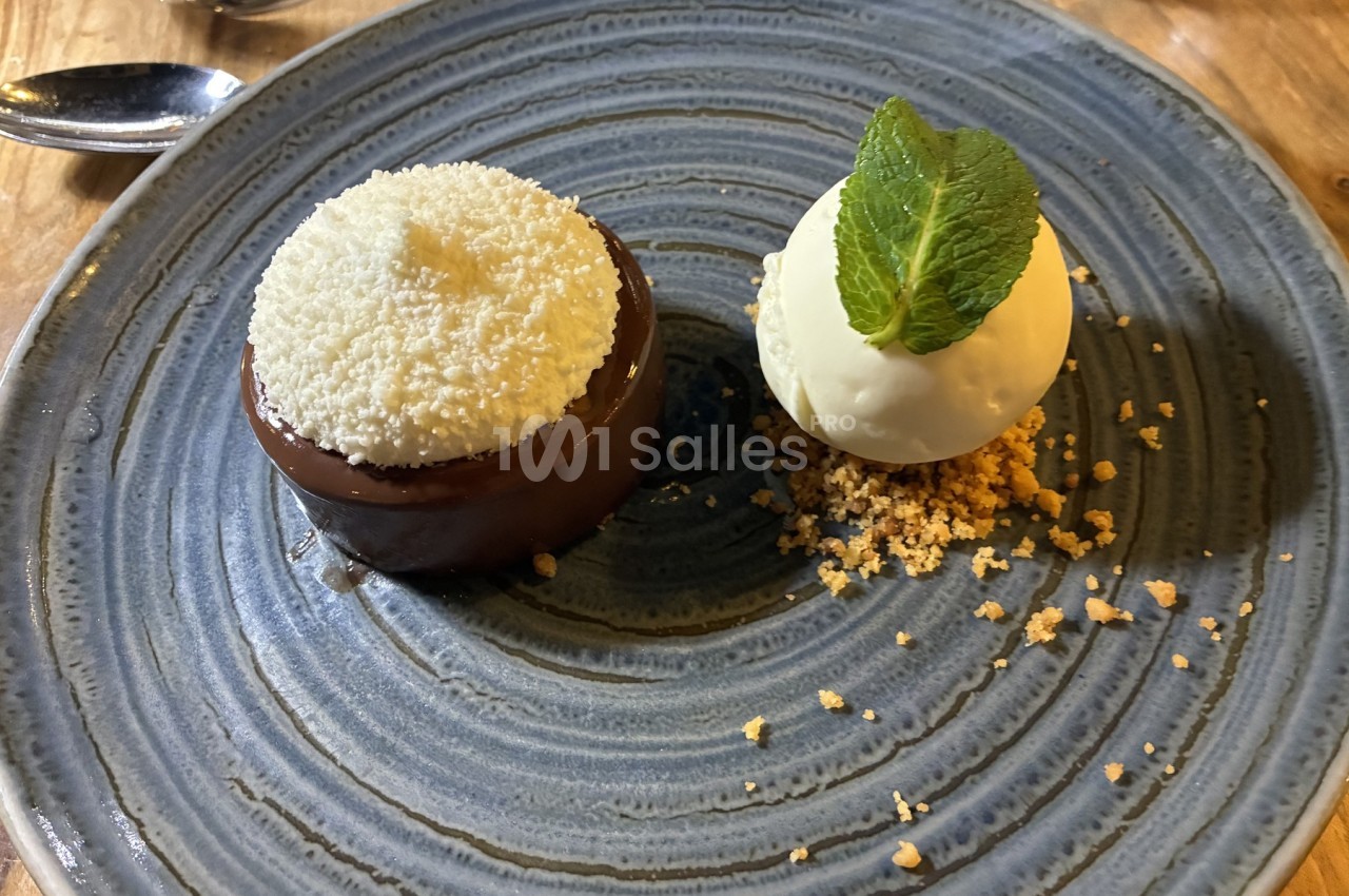 Dessert composé d'un gâteau au chocolat avec une garniture blanche et d'une boule de glace sur un lit de crumble.