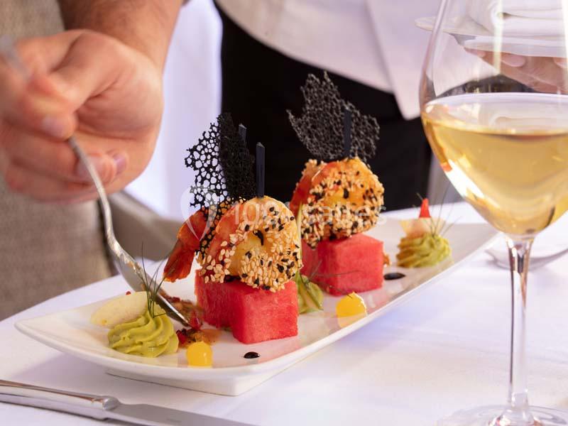 Assiette gastronomique avec crevettes, pastèque, mousse d'avocat et décorations, servie sur une table élégante.
