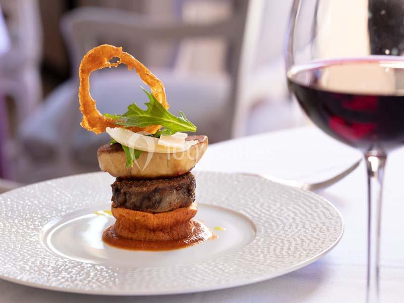 Assiette gastronomique avec une présentation soignée de viande, purée, légumes et un verre de vin rouge en arrière-plan.