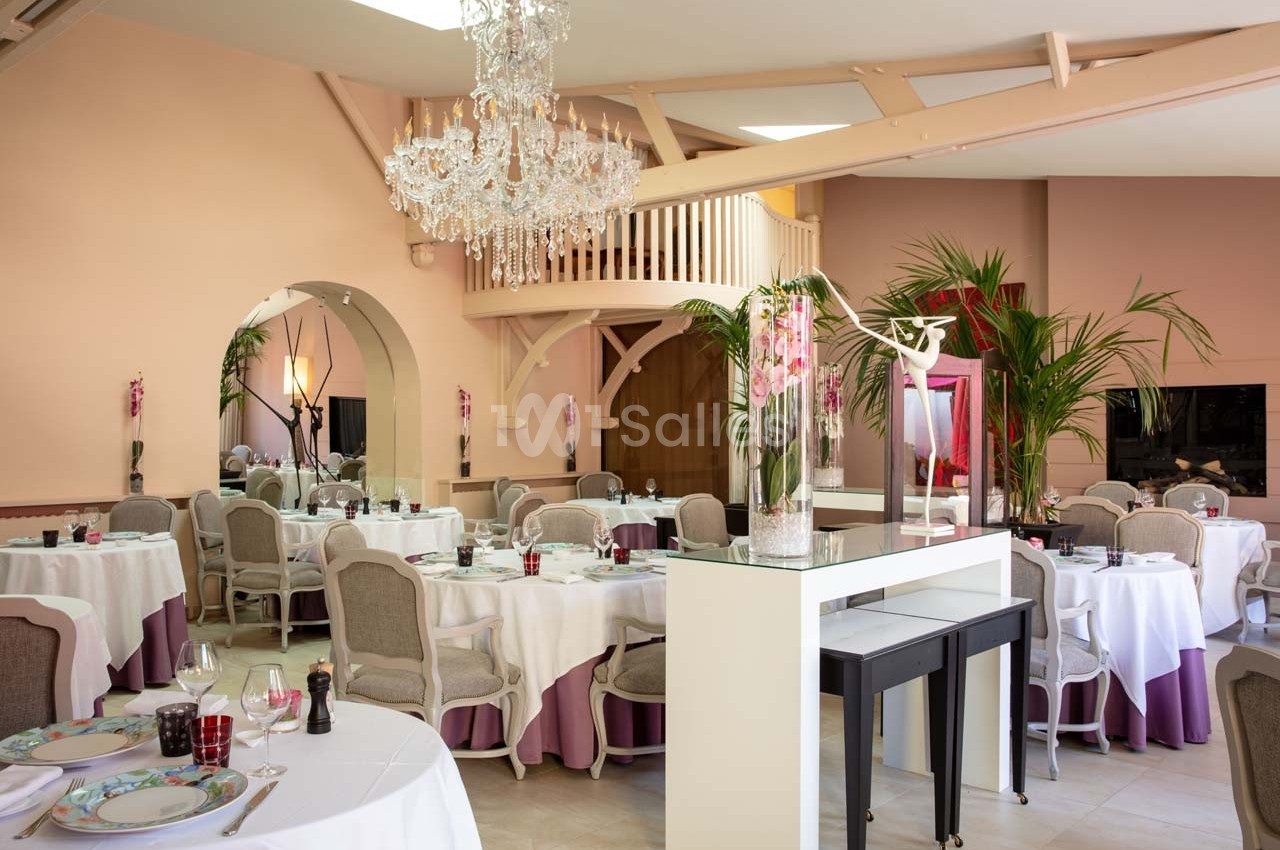 Salle de restaurant élégante avec tables dressées, chaises rembourrées, lustre en cristal et décoration végétale.