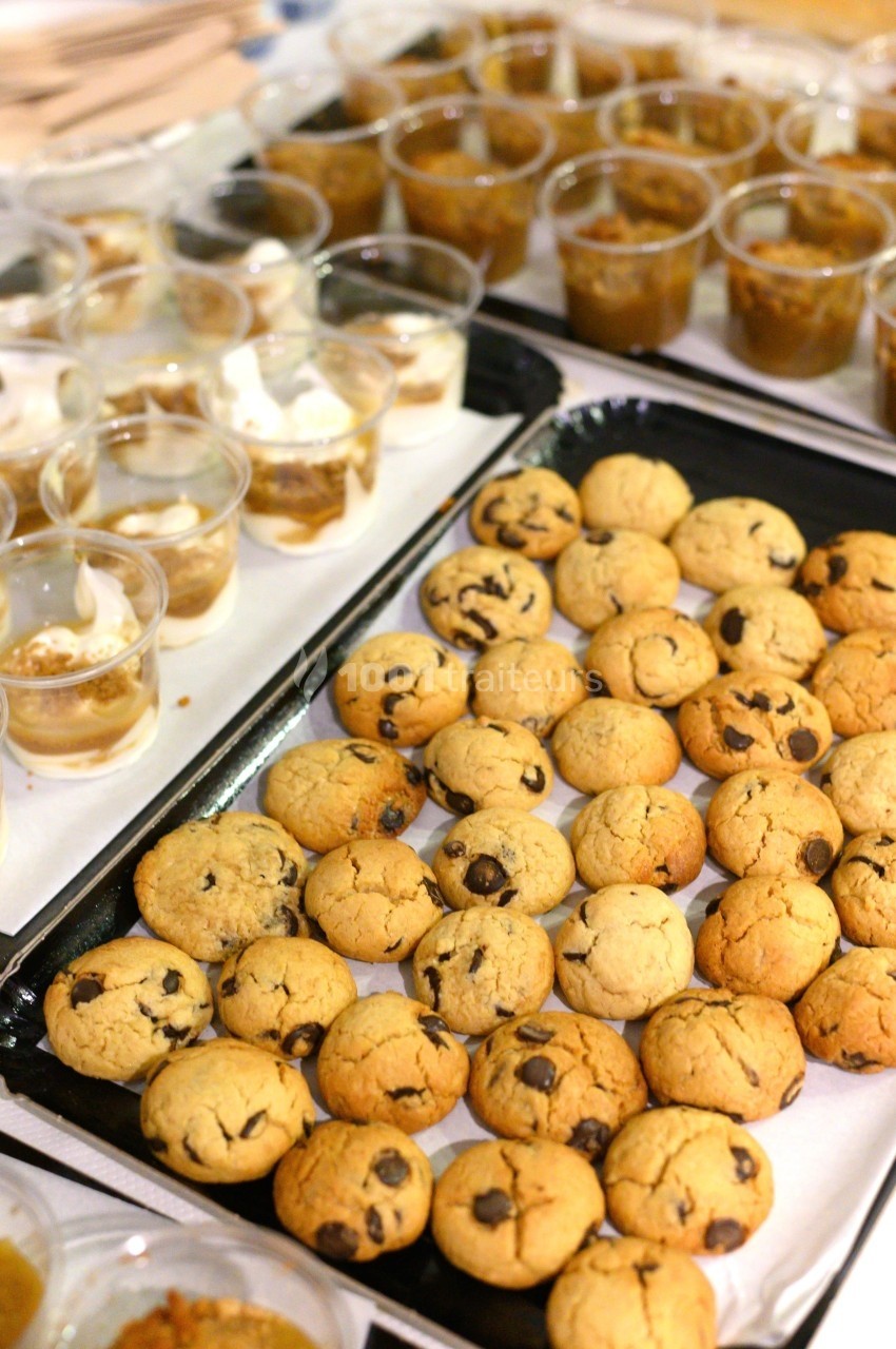 Plateau de cookies aux pépites de chocolat et verrines de dessert disposés sur une table.
