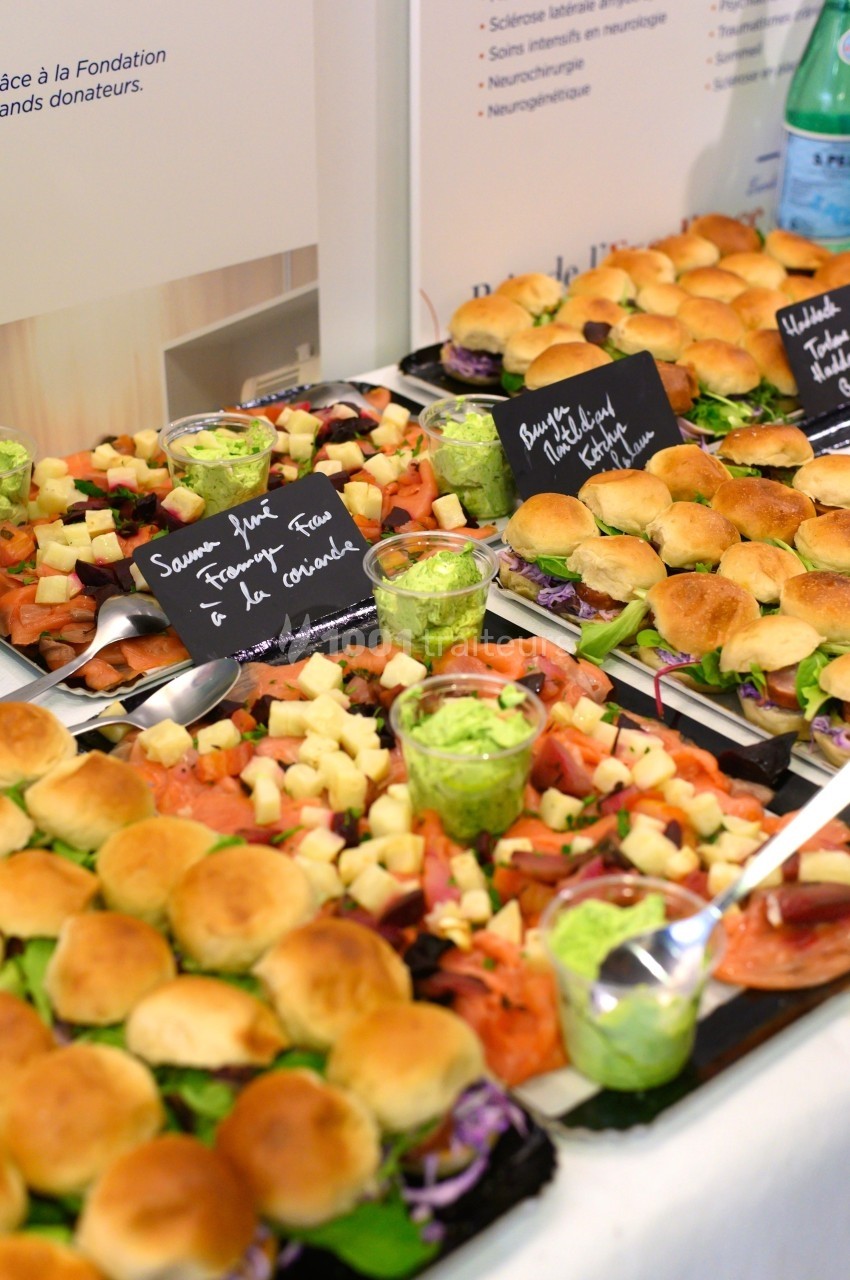 Plateaux de mini-sandwichs variés avec garnitures, accompagnés de verrines de sauce verte et étiquettes descriptives.