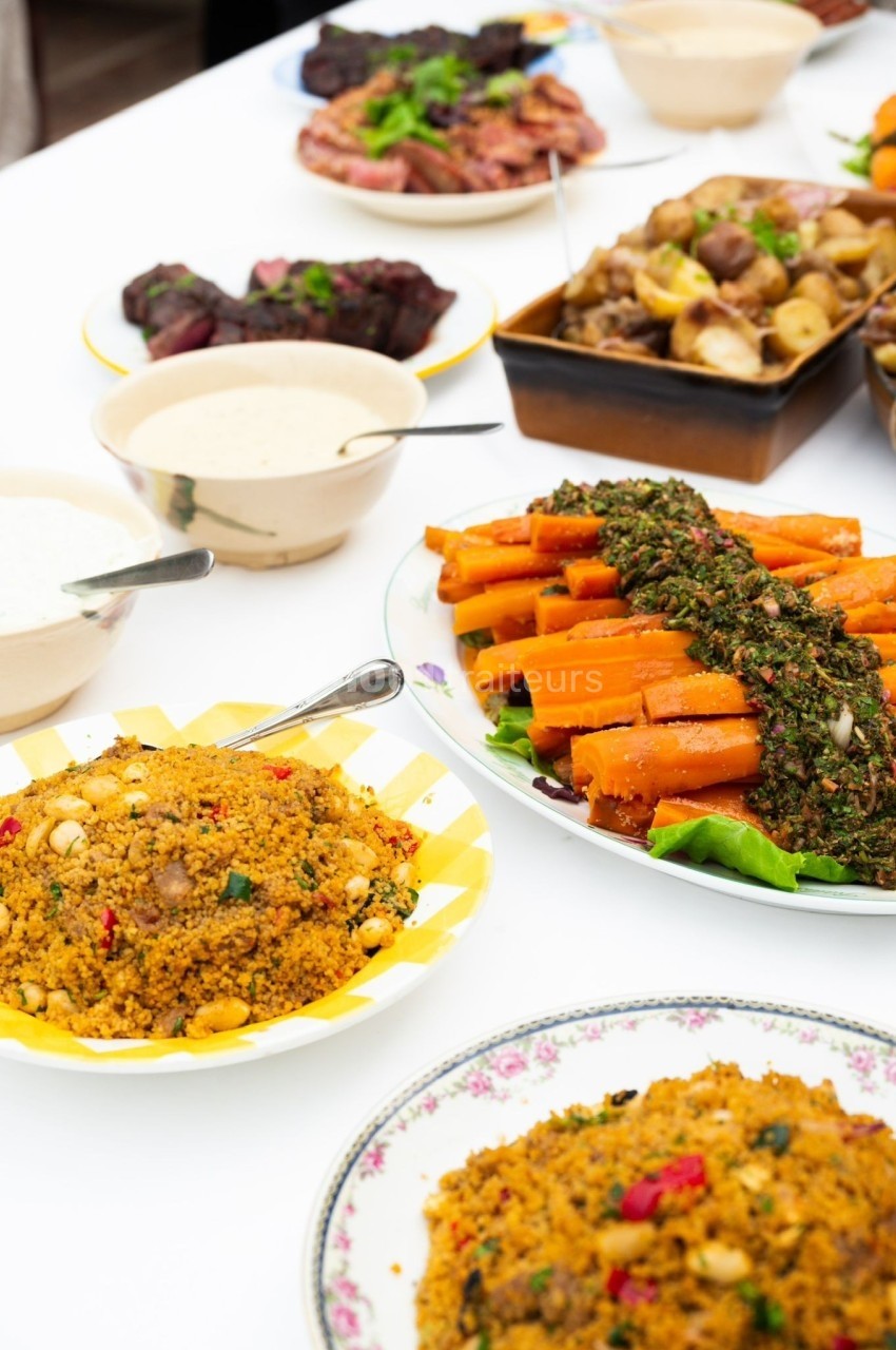 Assortiment de plats sur une table, incluant carottes garnies, semoule épicée et accompagnements variés.