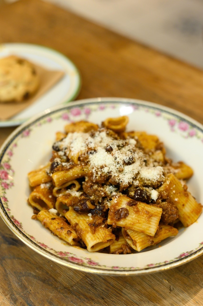 Assiette de rigatoni à la sauce bolognaise garnie de fromage râpé, posée sur une table en bois.