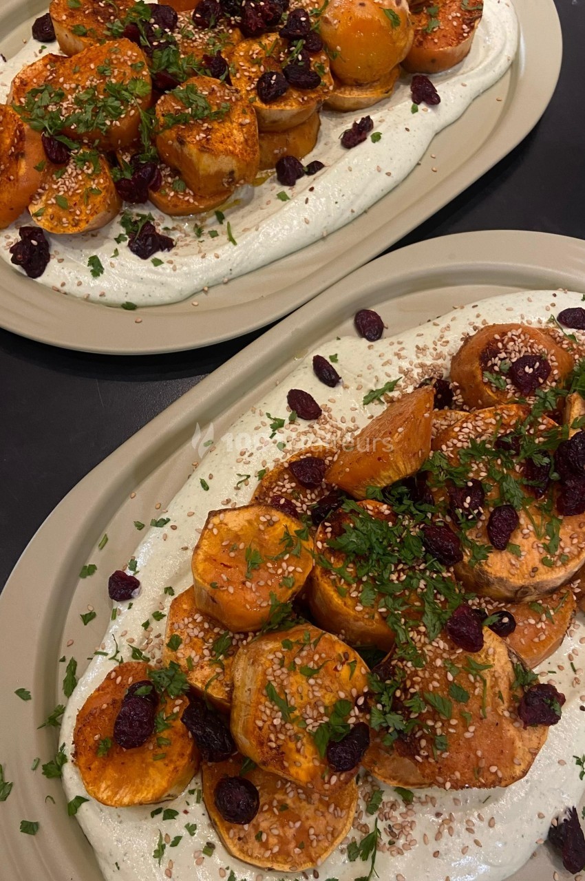 Assiette de patates douces rôties garnies de yaourt, herbes fraîches, graines de sésame et cranberries séchées.