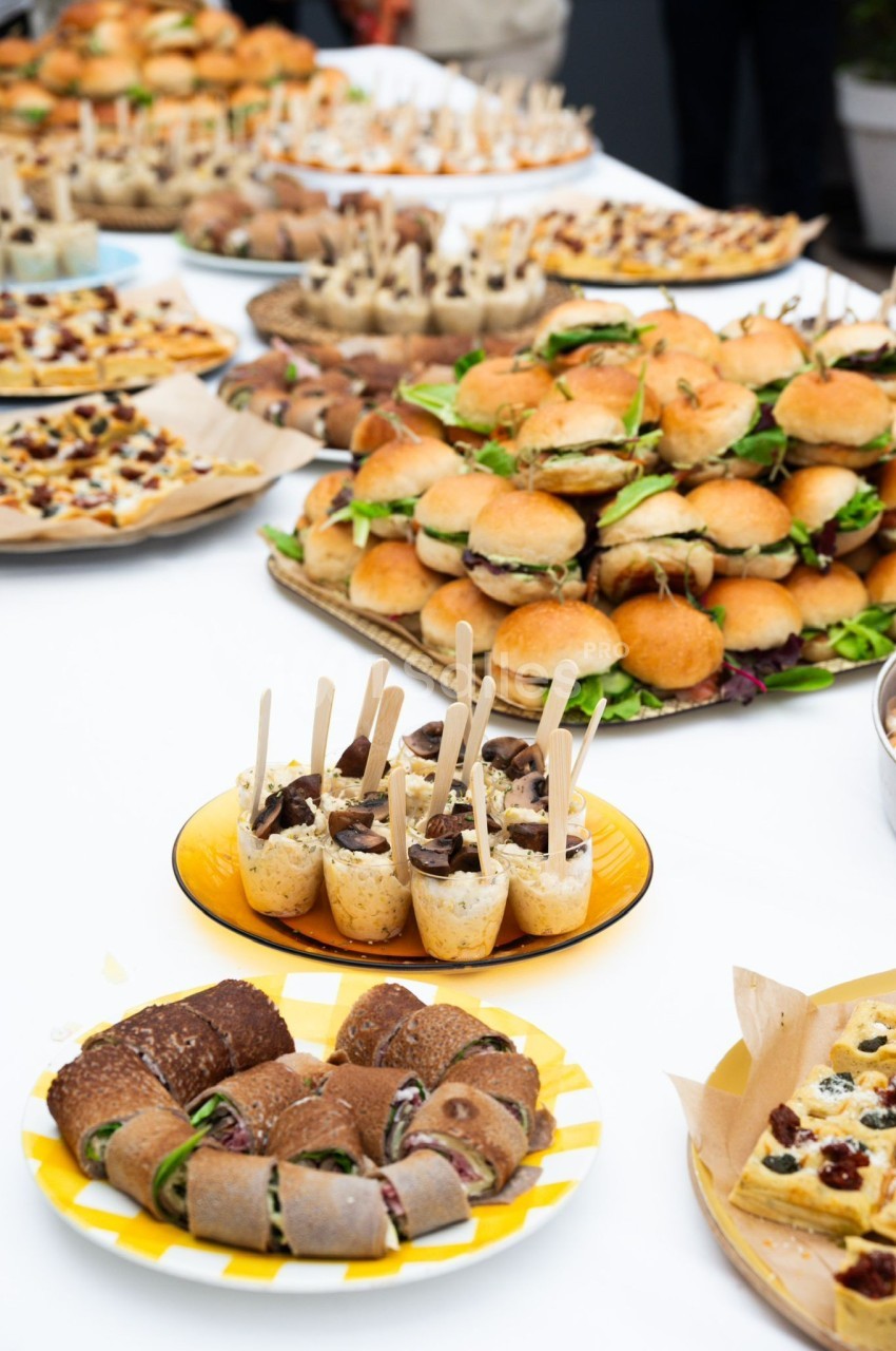 Buffet avec mini-sandwichs, roulés, verrines et autres amuse-bouches disposés sur une table blanche.