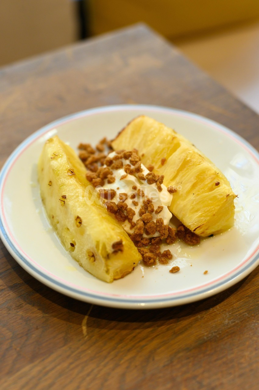 Tranches d'ananas frais servies avec une garniture de crème et des éclats de noix sur une assiette blanche.