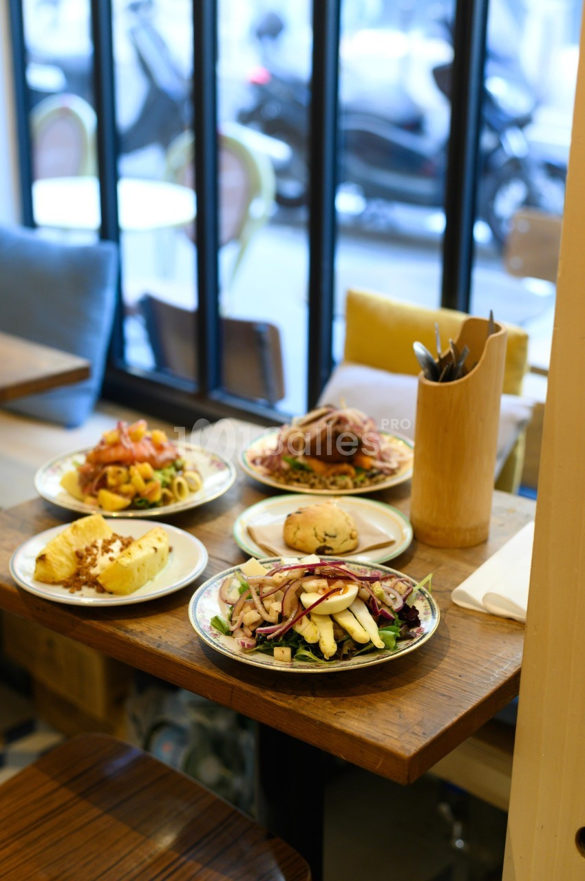 Assortiment de plats servis sur une table en bois dans un restaurant, avec une vue sur la rue à travers une baie vitrée.